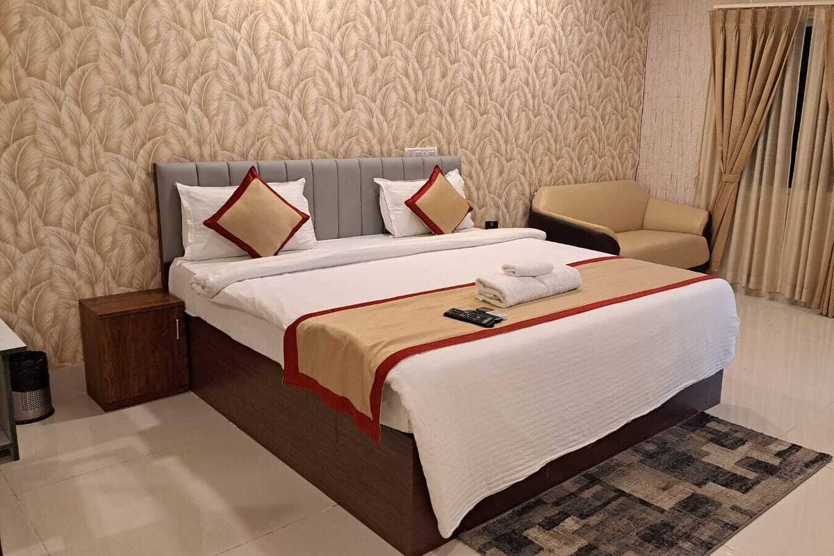 Una habitación de hotel con una cama grande, una silla, una mesita de noche y un papel tapiz estampado.