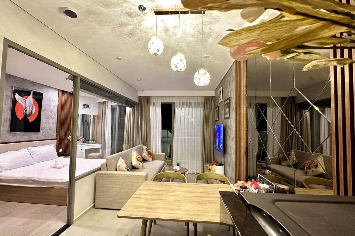 A modern hotel room with a bed, sofa, dining table, and TV.