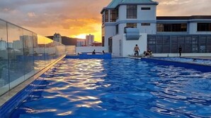 Piscina en la azotea con barandilla de vidrio y vistas a la puesta de sol y al paisaje urbano.