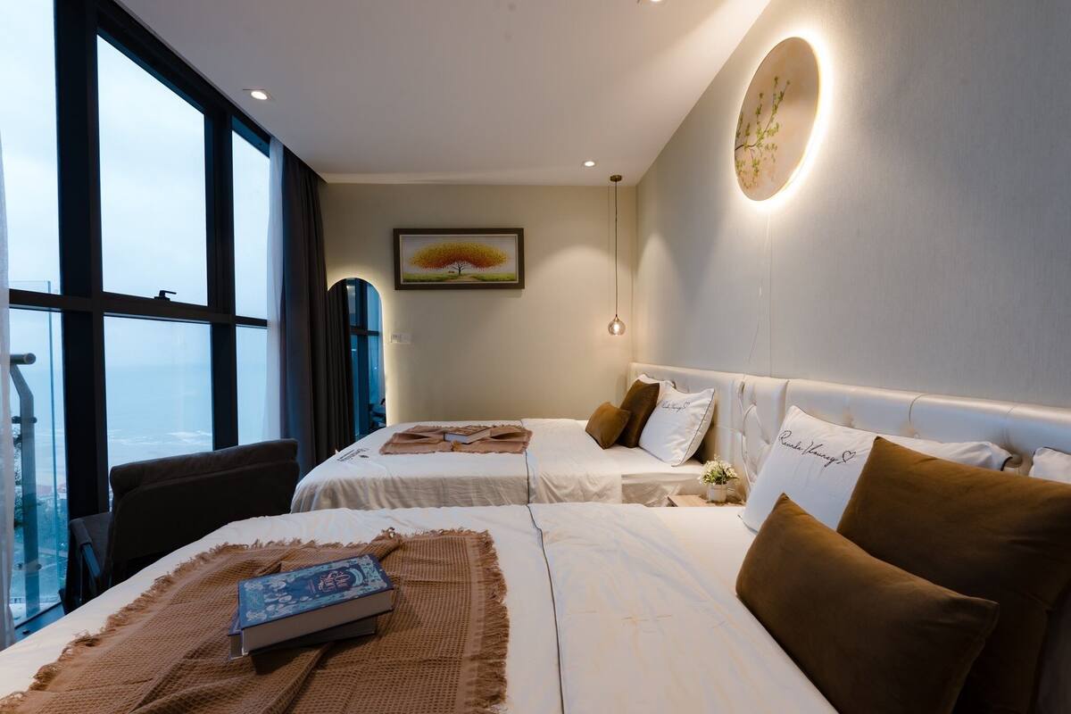 A hotel room with two beds, a large window, a painting, and a wall-mounted light fixture.