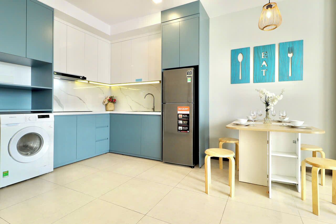 A modern kitchen with a washing machine, a refrigerator, and a dining area with stools.