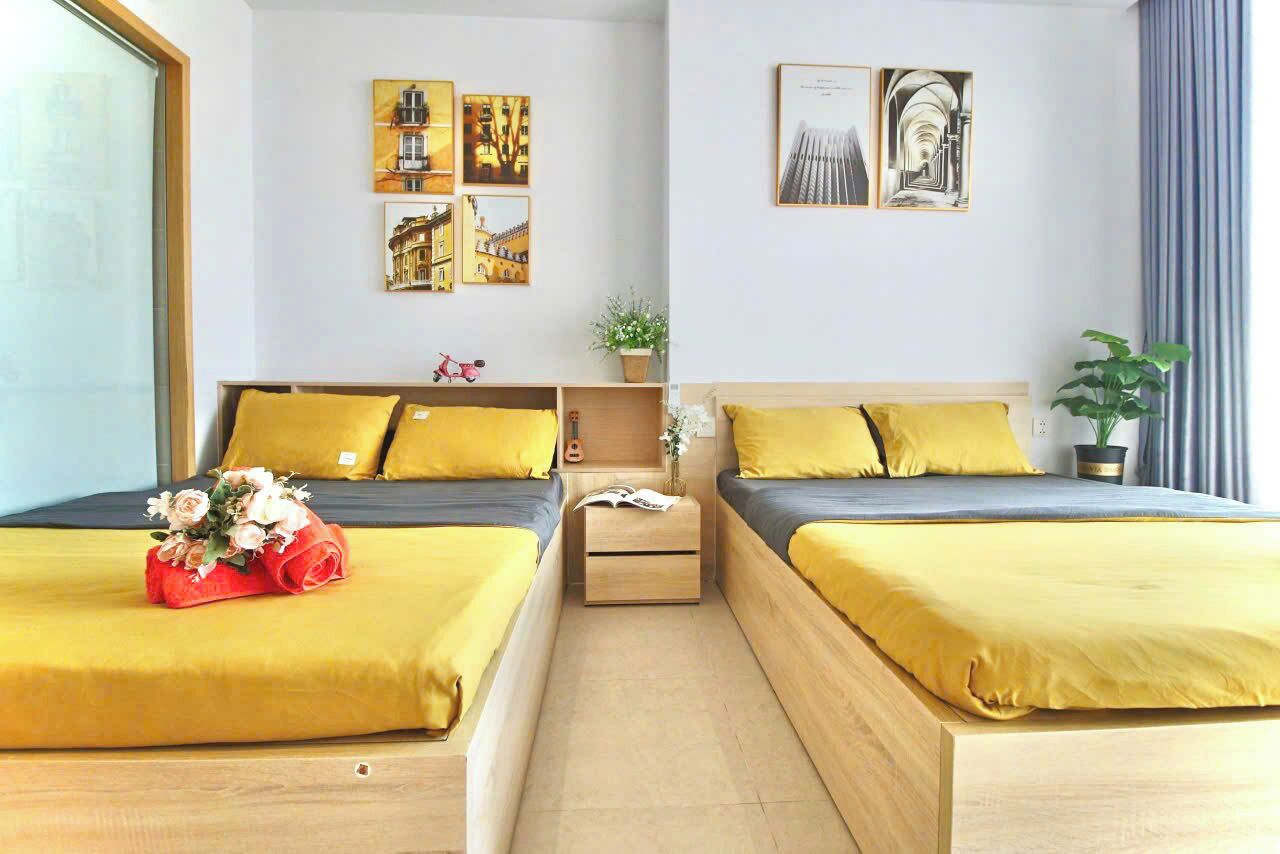 A hotel room with two beds, each with yellow bedding, a small bedside table with a plant, and artwork on the walls.