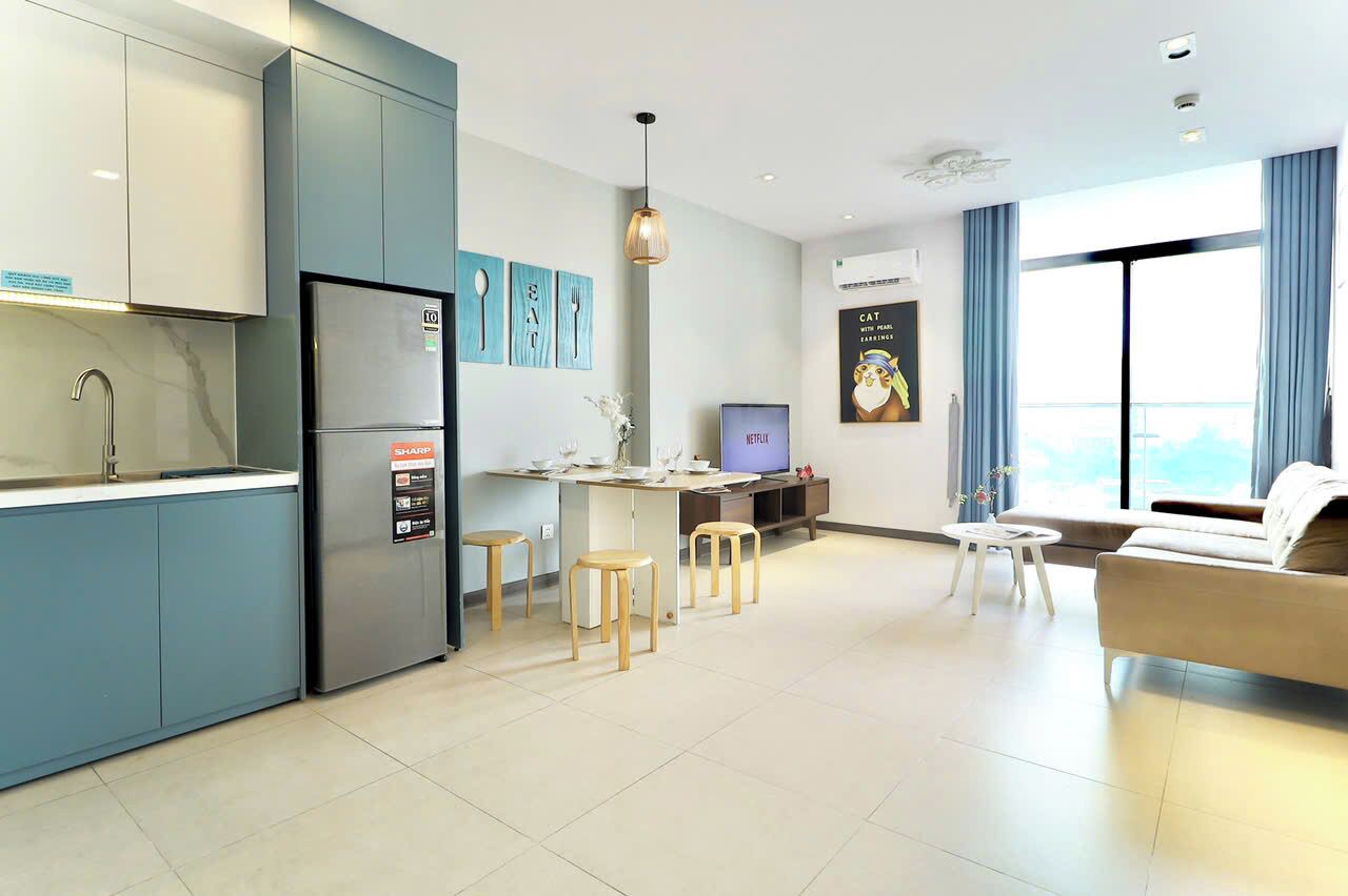 A modern kitchen with a refrigerator, dining area with stools, a TV, and a sofa.