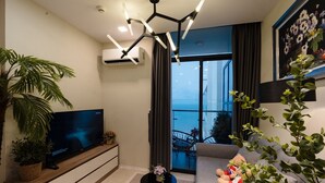 Una sala moderna con una televisión de pantalla plana, una lámpara en el techo, una planta en maceta, un sofá con un oso de peluche y un balcón con vistas.