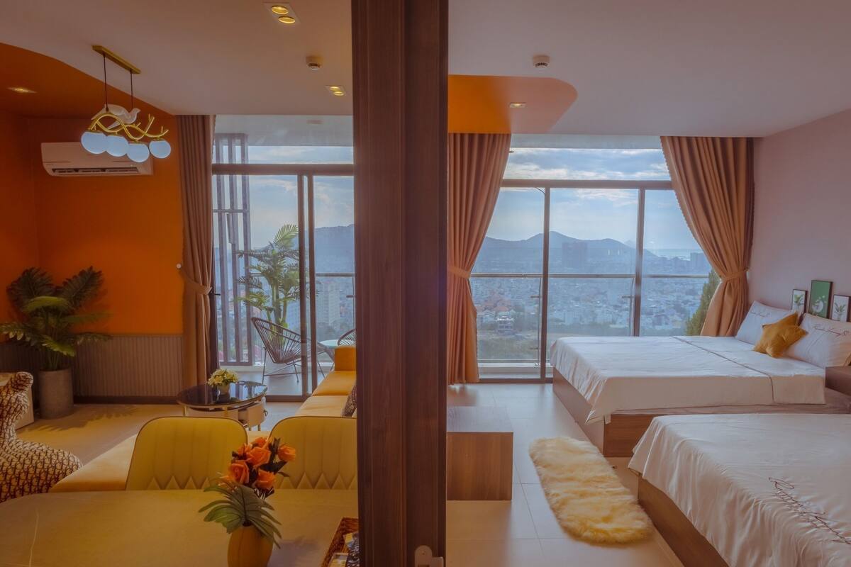 A hotel room with two beds, a sofa, a dining table, and a view of the city.