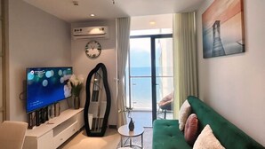 Una sala moderna con un sofá verde, un televisor de pantalla plana, un espejo grande y vista al océano a través de un ventanal.