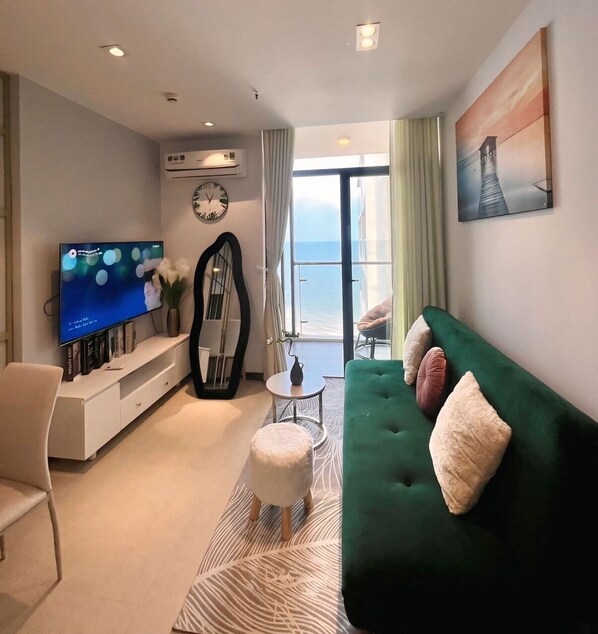 Una sala moderna con un sofá verde, un televisor de pantalla plana, un espejo grande y vista al océano a través de un ventanal.