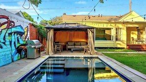 A backyard with a swimming pool, a covered seating area, and a graffiti-covered wall. - Pool & Vibes, Relaxing and Fun! (Austin)