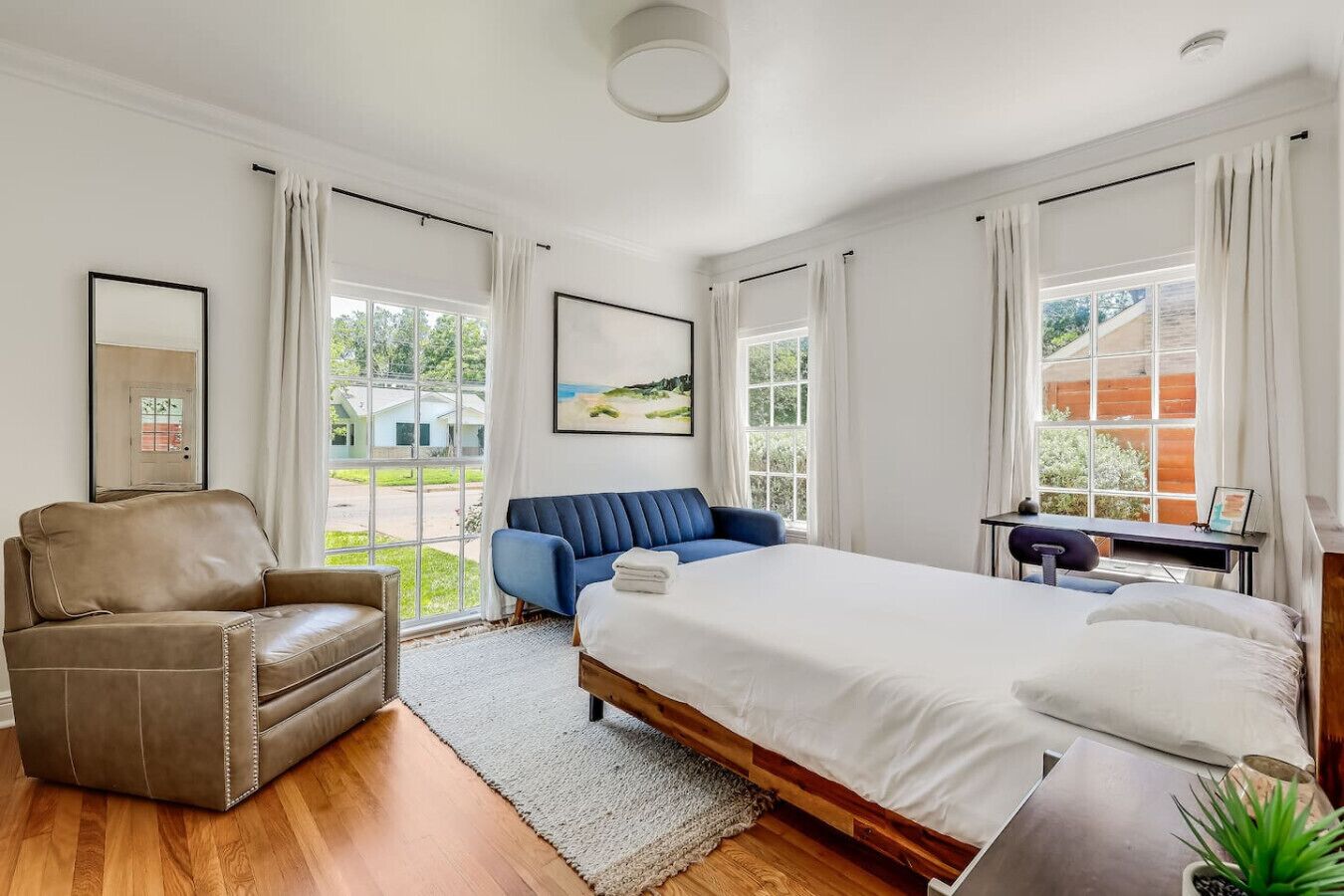 Ein Schlafzimmer mit Bett, Schreibtisch, Stuhl und großen Fenstern.