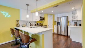 Una cocina moderna con una isla central, taburetes de bar, electrodomésticos de acero inoxidable y un letrero de neón.