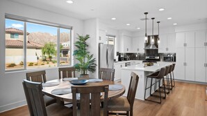 A modern kitchen with white cabinets, a central island with bar stools, and a dining area with a round table and chairs. - PGA Signature at its FINEST, Steps to resort, Game Room, Luxe Interior (La Quinta)
