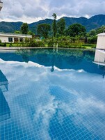 A clear blue pool with a tiled floor, surrounded by lush greenery and mountains in the background.