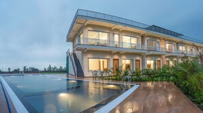 Un hôtel moderne à plusieurs étages, doté d’une piscine, de balcons et d’un jardin bien entretenu.