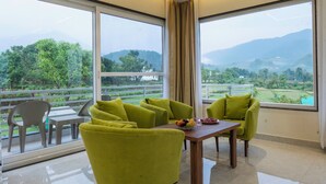 A room with a balcony, a dining table, and green chairs. - Corbett Four Seasons (Ramnagar)