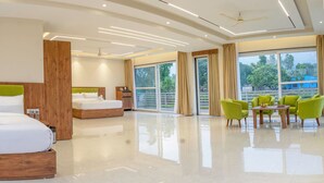 A modern hotel room with a large bed, a smaller bed, and a seating area with green chairs. - Corbett Four Seasons (Ramnagar)