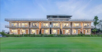 A modern multi-story building with a flat roof, large windows, and a well-maintained lawn in front.