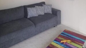 A grey sofa with patterned cushions, a colorful rug, and a ceiling fan. - Le Jasmyna (Sans Pareil)