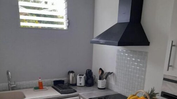 A compact kitchen with a dishwasher, sink, and a black range hood. - Le Jasmyna (Sans Pareil)