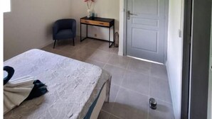 A bedroom with a bed, a desk, a chair, and a door. - Le Jasmyna (Sans Pareil)
