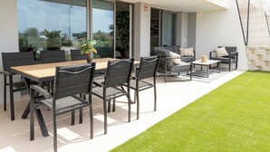 A modern outdoor dining area with a wooden table and black chairs, a small coffee table, and a sofa with cushions.
