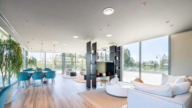 A modern living room with a large window, a dining area with blue chairs, and a white sofa.