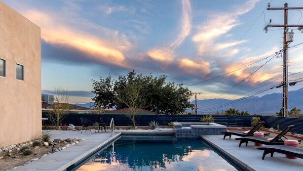 A rectangular swimming pool with a tiled deck, surrounded by lounge chairs and a patterned rug.