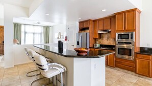 A modern kitchen with a large island, wooden cabinets, stainless steel appliances, and a bar area with bar stools.