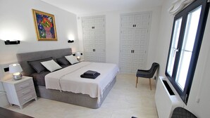 Une chambre à coucher avec un lit, des tables de chevet, une chaise, un bureau et une fenêtre.