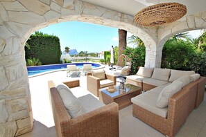 A sunlit outdoor seating area with wicker furniture, a pool, and a stone archway. - Relaxa - modern Villa with pri. pool & sea views in Benissa (Benissa)