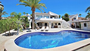 Une piscine à bords incurvés, entourée d’une terrasse aménagée avec des chaises longues et un palmier.