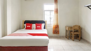 Un dormitorio con cama, aire acondicionado, ventana con cortinas, un escritorio de madera y una silla.