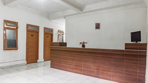 Un área de recepción con un mostrador de madera, tres puertas de madera, piso de baldosas y una pequeña planta en maceta.