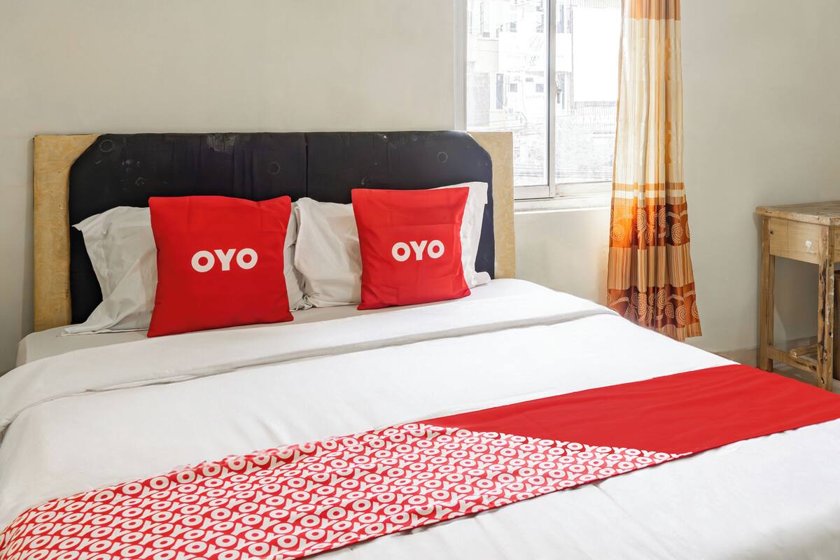 A bed with a white and red patterned bedspread, two red pillows with "OYO" text, and a wooden headboard.