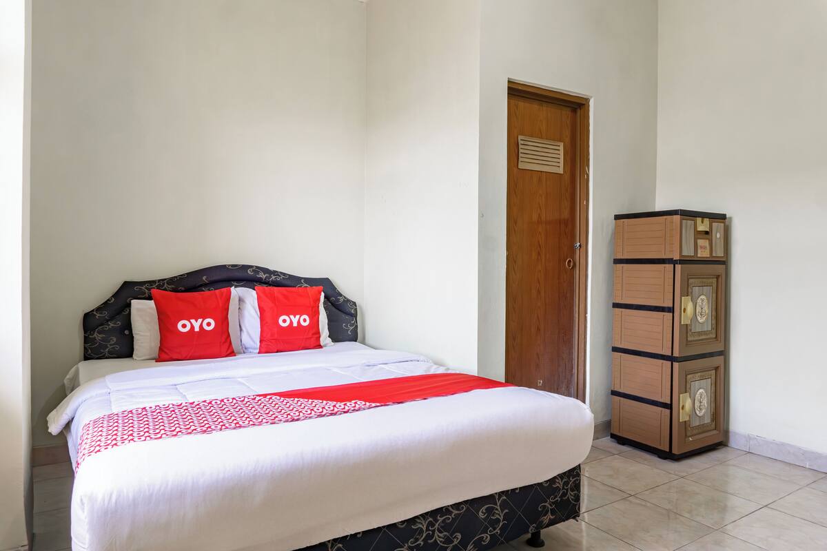 A neatly made bed with a white and red bedspread, two red pillows with the word "OYO" on them, and a wooden cabinet with multiple drawers to the right.