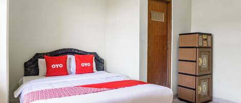 A neatly made bed with a white and red bedspread, two red pillows with the word "OYO" on them, and a wooden cabinet with multiple drawers to the right.