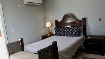 Quarto com cama, mesa de cabeceira, luminária, cadeira e ar condicionado.