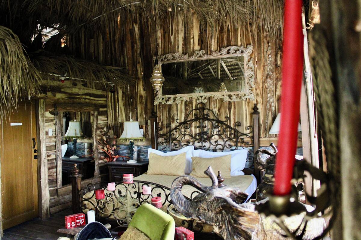 Een landelijke kamer met een bed, een nachtkastje, een lamp en een decoratieve spiegel.