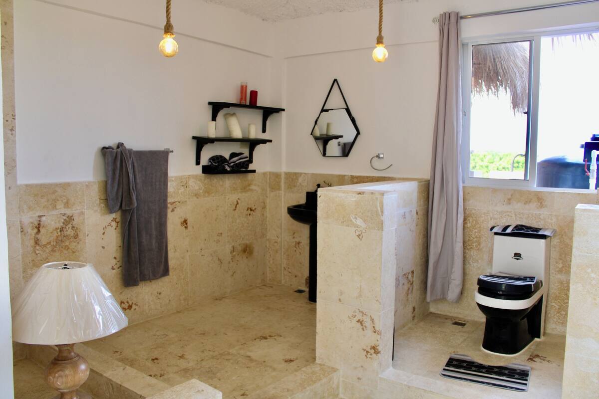 Een badkamer met een bad, toilet, wastafel en spiegel. Twee plankjes met toiletartikelen en een handdoek hangen aan de muur.