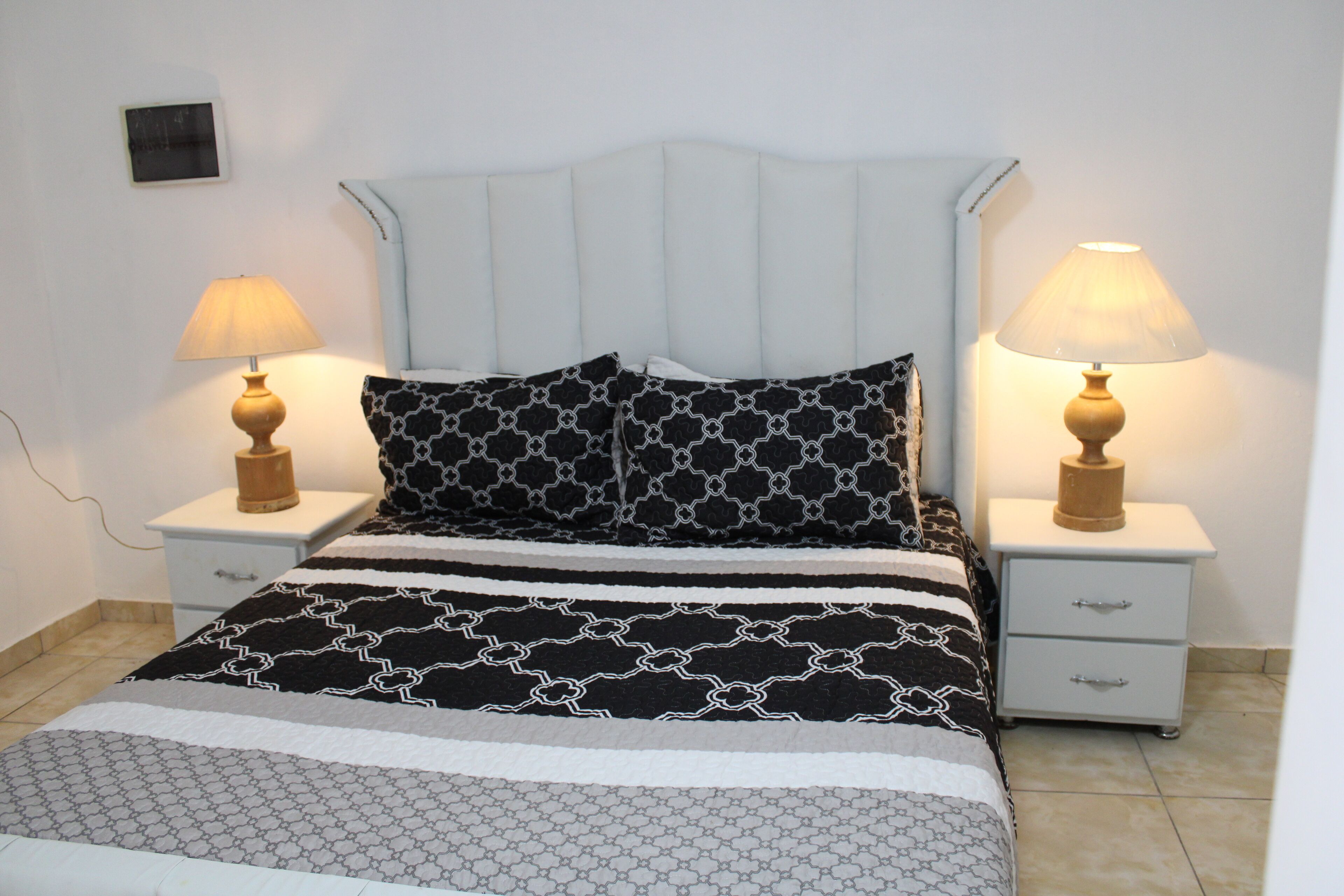 Een net opgemaakt bed met beddengoed met een patroon, twee nachtkastjes met lampen, en een klein nachtkastje.