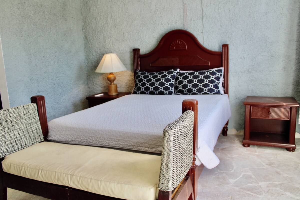 Een keurig opgemaakt slaapkamer met een bed, twee nachtkastjes, een lamp en een stoel.