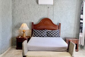 A bedroom with a wooden headboard, a bedside table with a lamp, a bed with patterned pillows, and a small nightstand. - Complejo Guayacanes (Guayacanes)