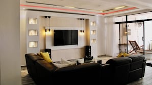 A modern living room with a large flat-screen TV, a glass coffee table, and a black leather sofa. - Complejo Guayacanes  (Guayacanes)