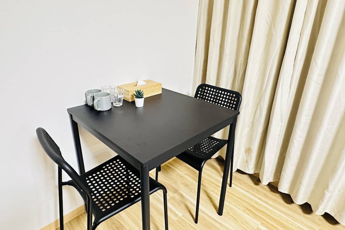 A small, dark-colored table with two black chairs, a tissue box, a small potted plant, and three gray mugs.
