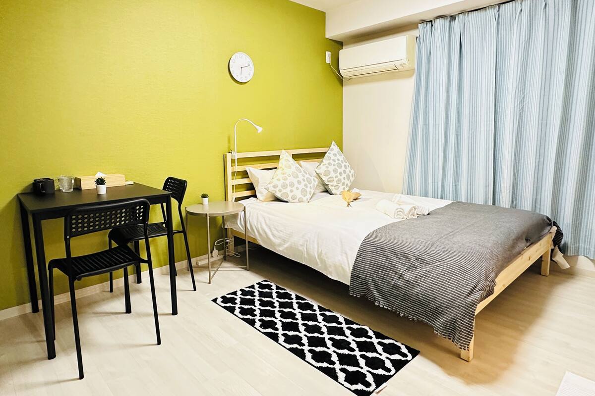A small, bright room with a bed, a desk, and a chair.