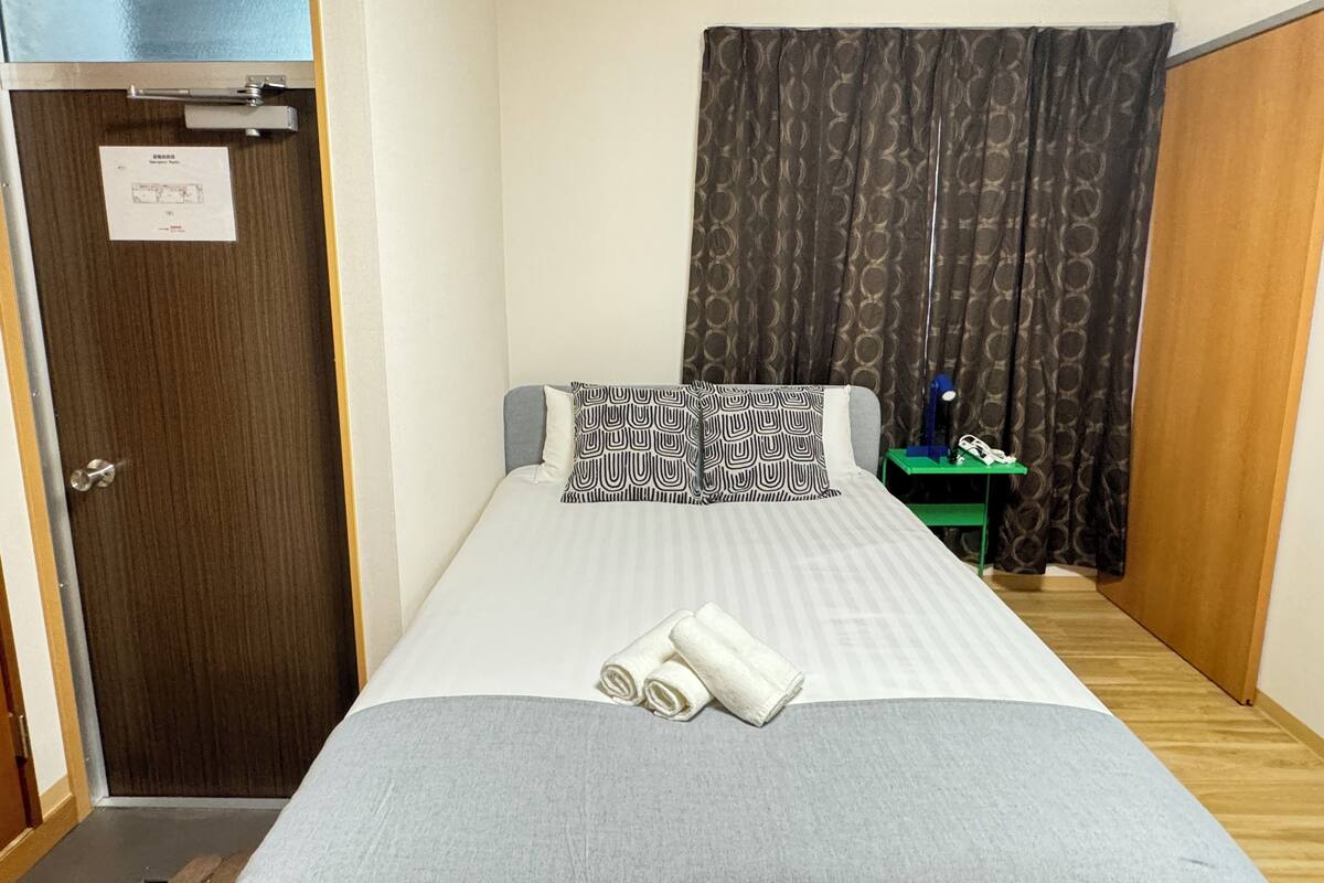 A small, neatly arranged bedroom with a single bed, a nightstand, a lamp, and a door with a sign.