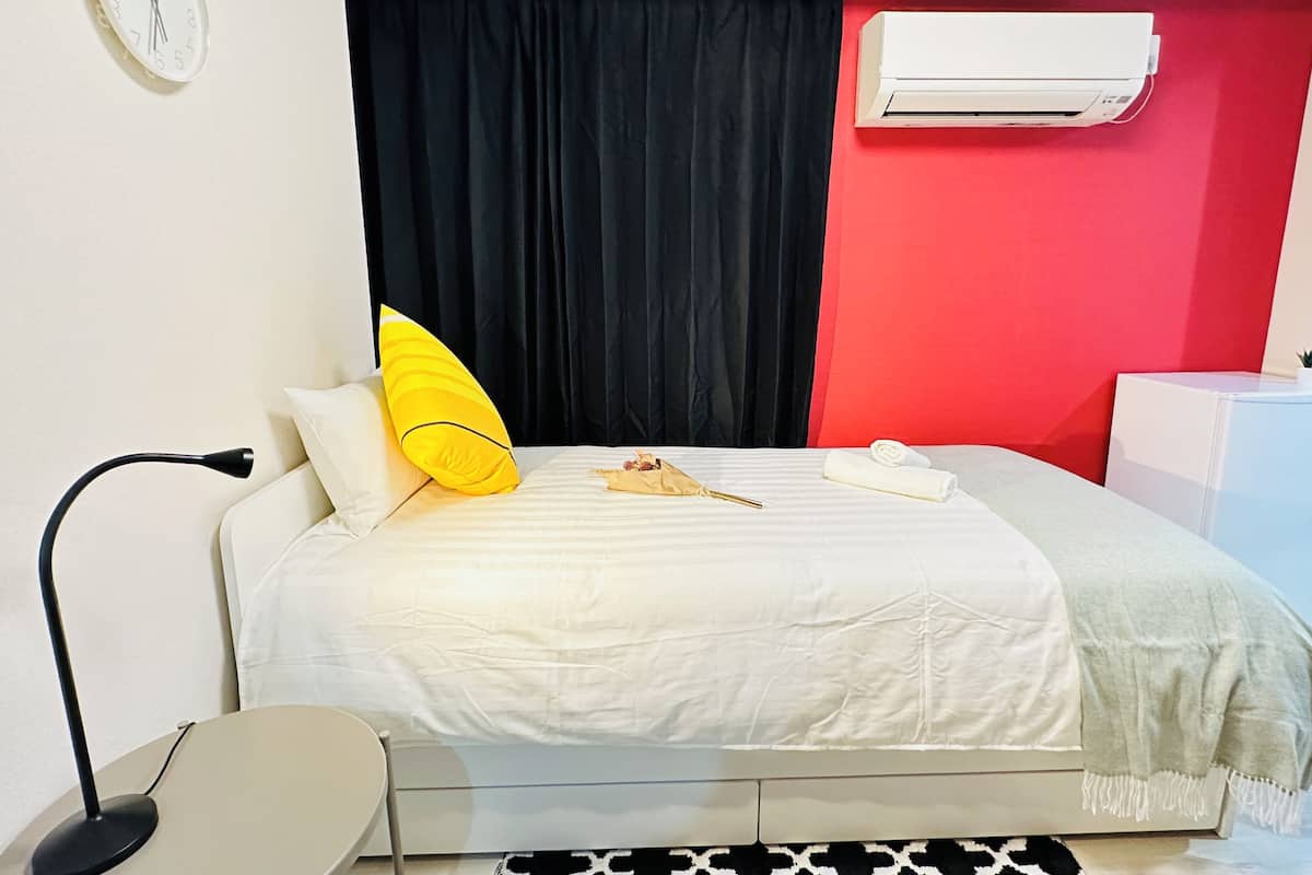 A bedroom with a bed, a black curtain, a white air conditioner, and a clock on the wall.