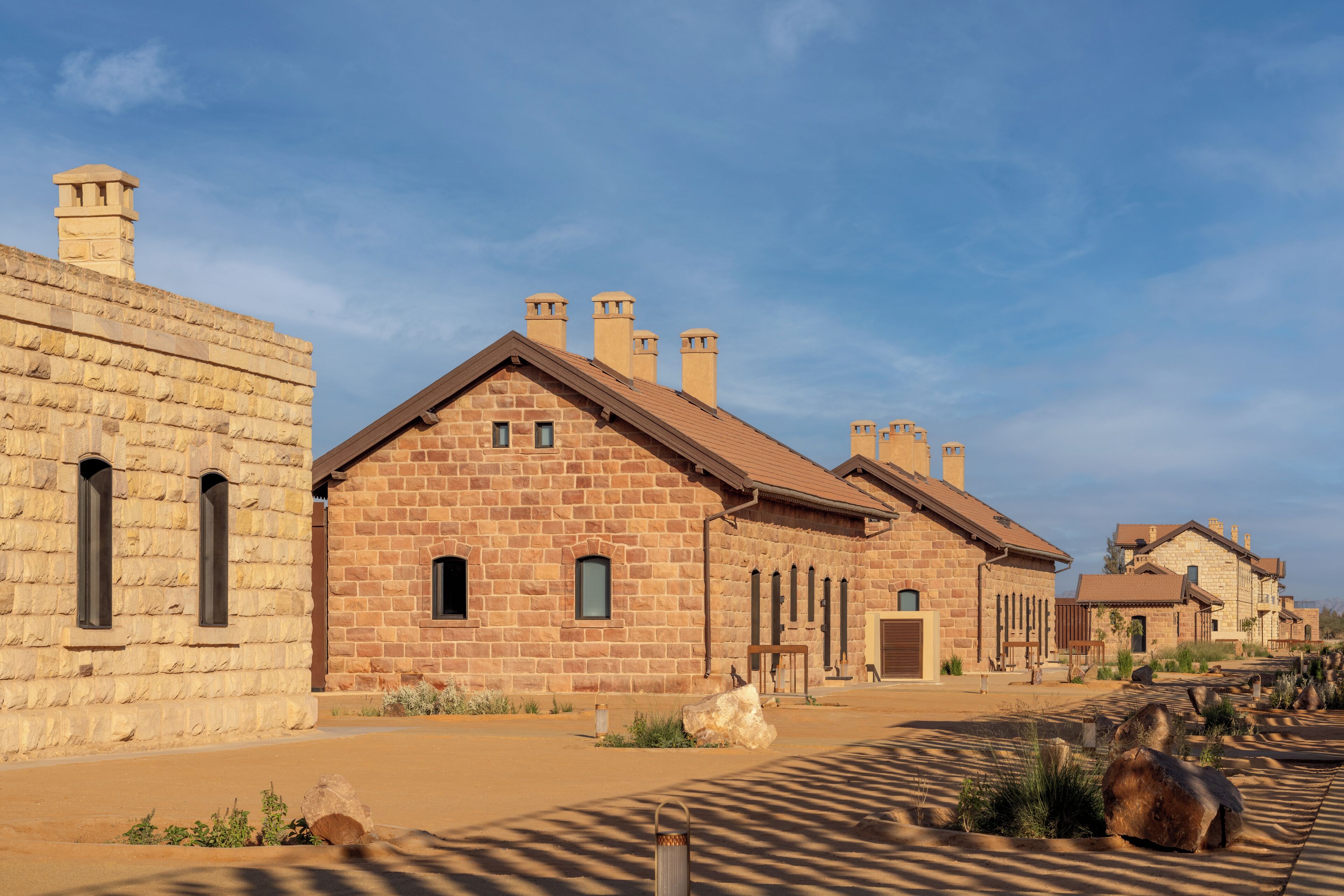 A row of stone buildings with a consistent architectural style, featuring multiple chimneys and a clear sky.