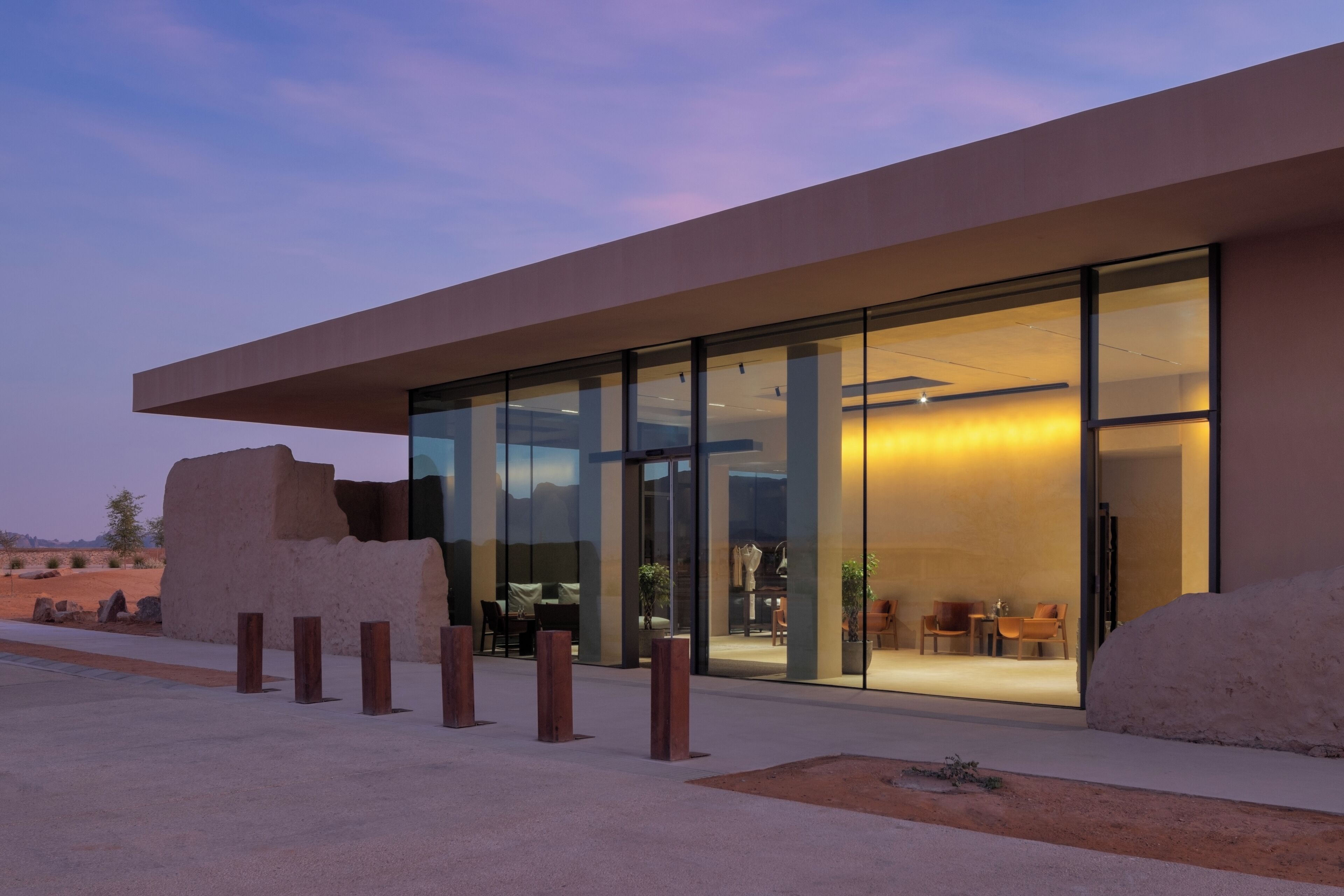 Un edificio moderno con amplias puertas de cristal, techo plano y un paisaje desértico al fondo.