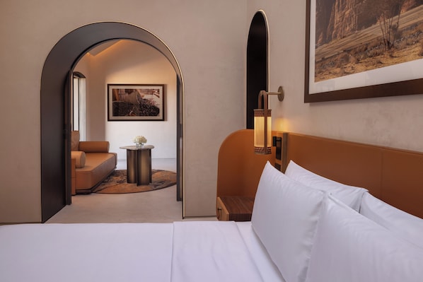 A hotel room with a bed, a sofa, a small table, and a painting on the wall.