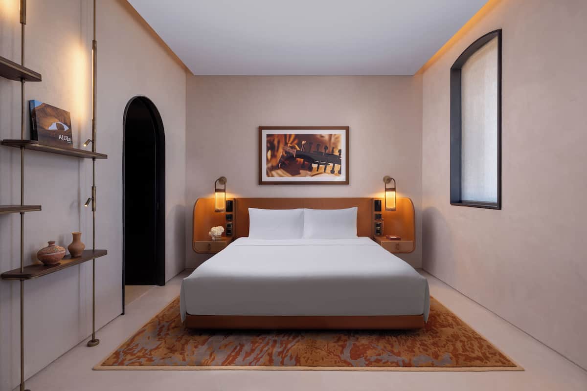 Habitació d'hotel moderna amb un llit gran, un capçal de fusta, un quadre encadre on la paret i una tauleta de nit amb una làmpada.
